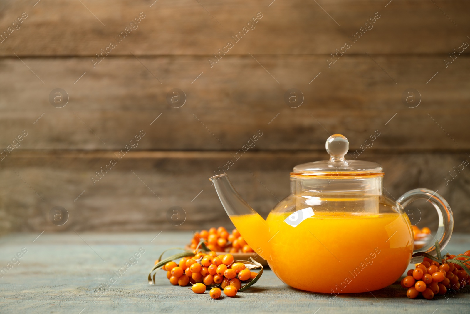 Photo of Delicious sea buckthorn tea and fresh berries on blue wooden table. Space for text