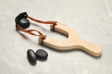 Photo of Wooden slingshot with stones on light grey marble background