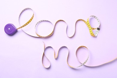 Photo of Phrase Love Me of measuring tape on pink background, top view