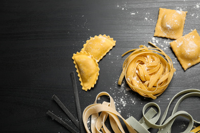 Flat lay composition with different types of pasta on black wooden table