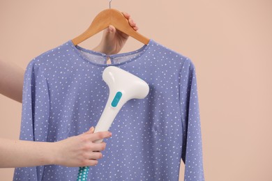 Photo of Woman steaming blouse on hanger against beige background, closeup