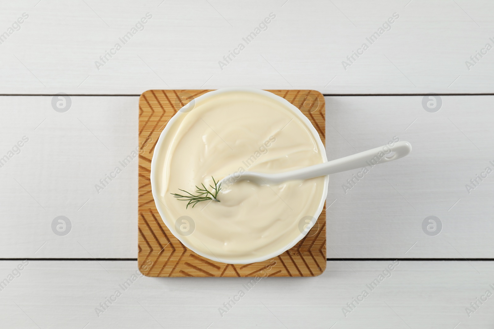 Photo of Fresh mayonnaise sauce in bowl on white wooden table, top view