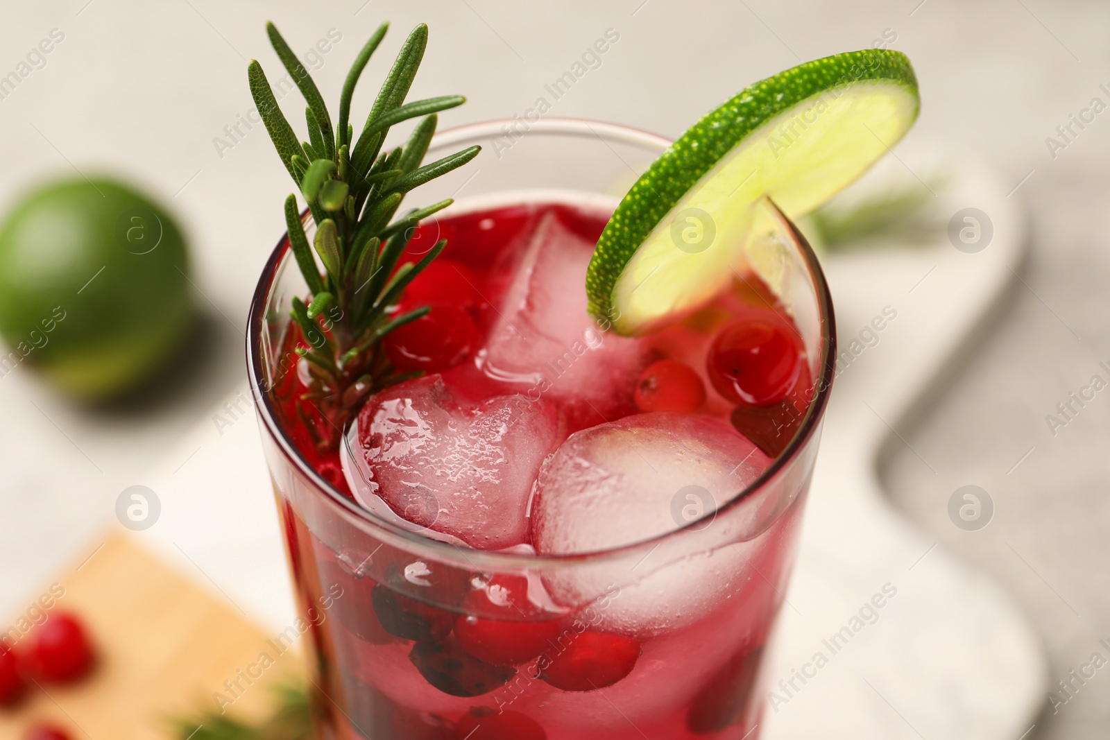 Photo of Tasty cranberry cocktail with rosemary and lime in glass on table, closeup