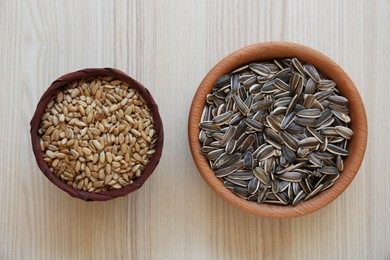 Photo of Bowls with organic sunflower seeds on white wooden table, flat lay