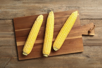 Tasty sweet corn cobs on wooden table, top view