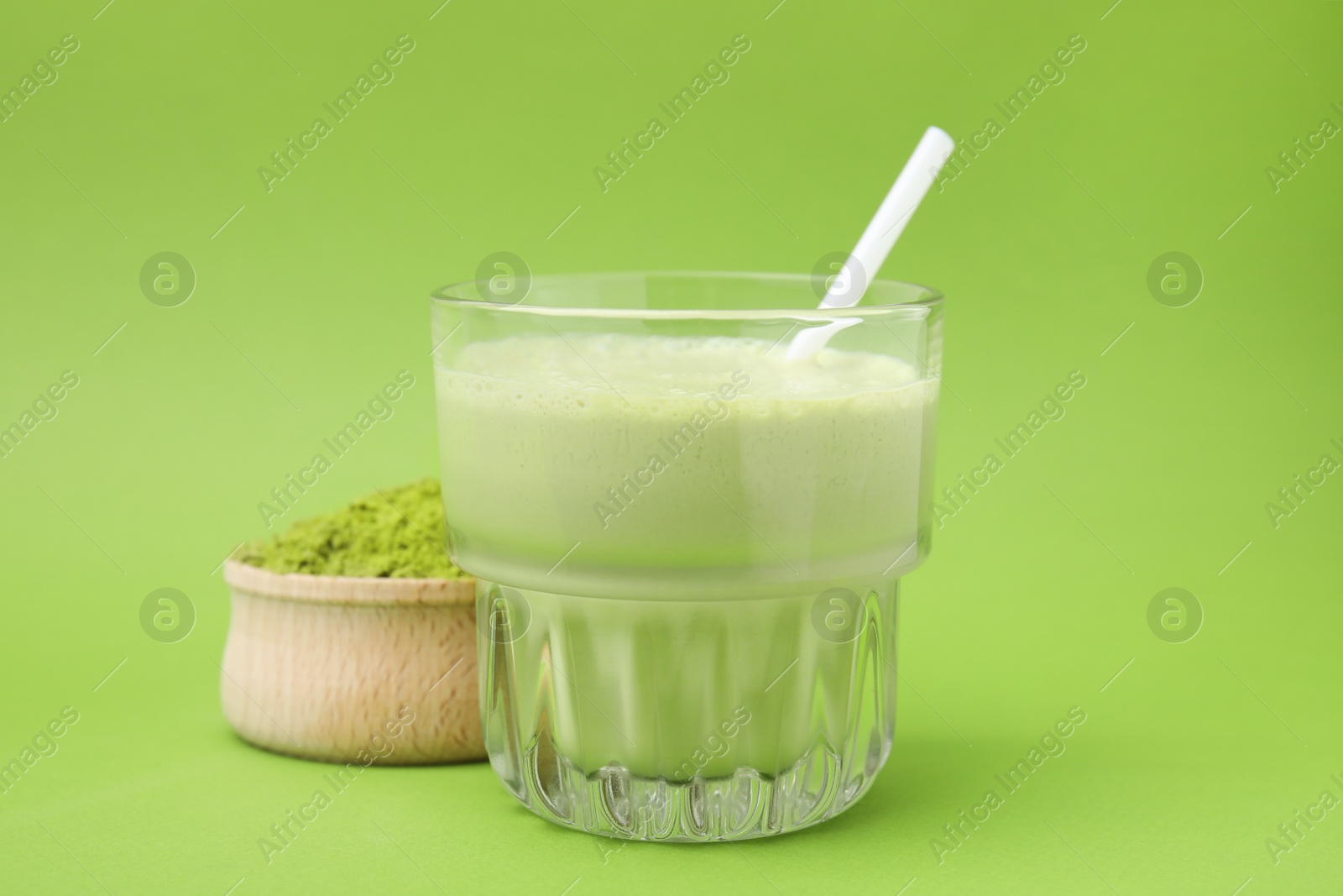 Photo of Glass of tasty matcha smoothie and powder on green background, closeup