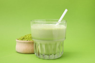 Glass of tasty matcha smoothie and powder on green background, closeup