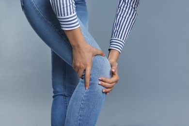 Photo of Woman suffering from knee pain on grey background, closeup