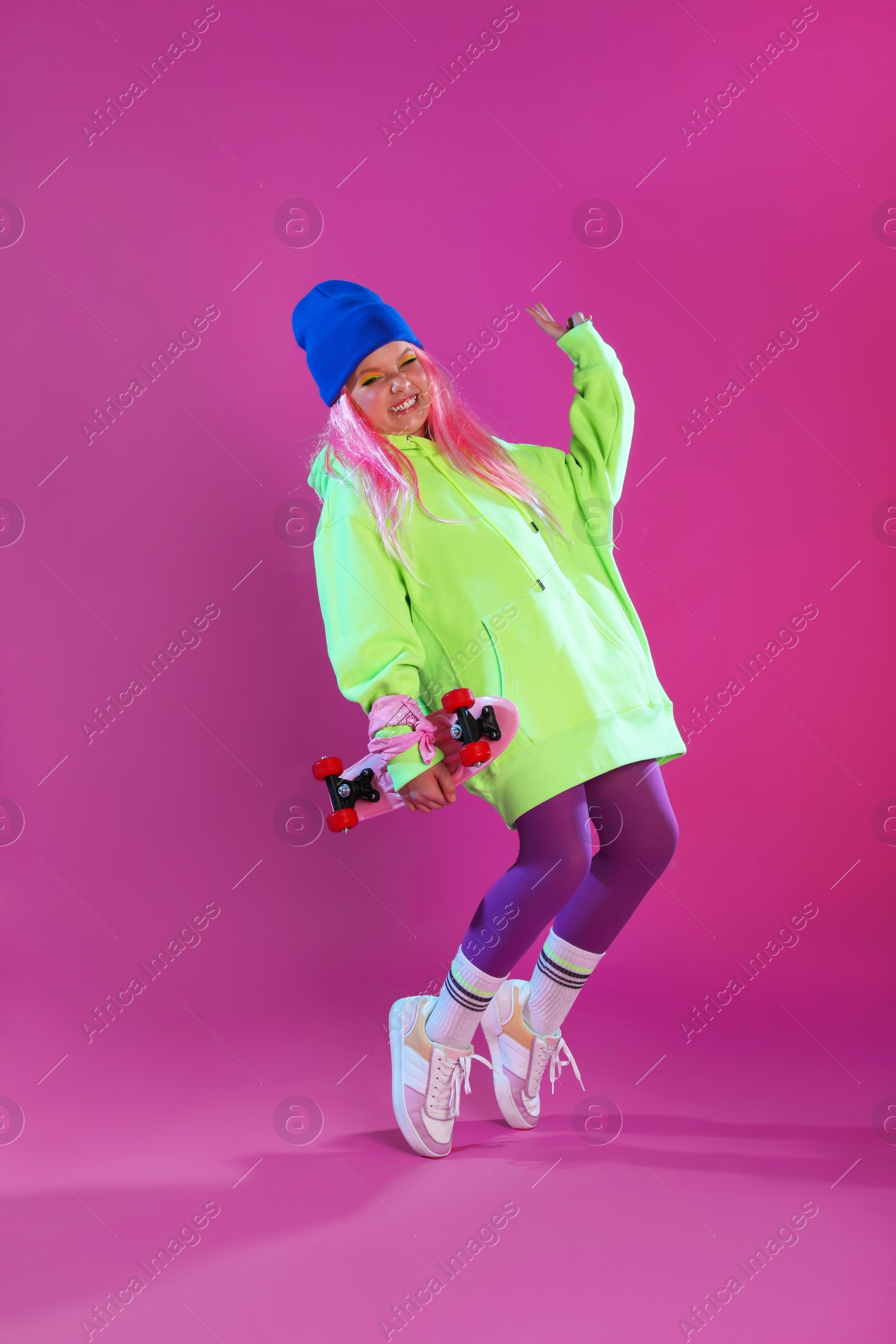 Photo of Cute indie girl with penny board on violet background