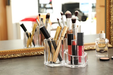 Lipstick holder with different makeup products on dressing table near mirror. Space for text