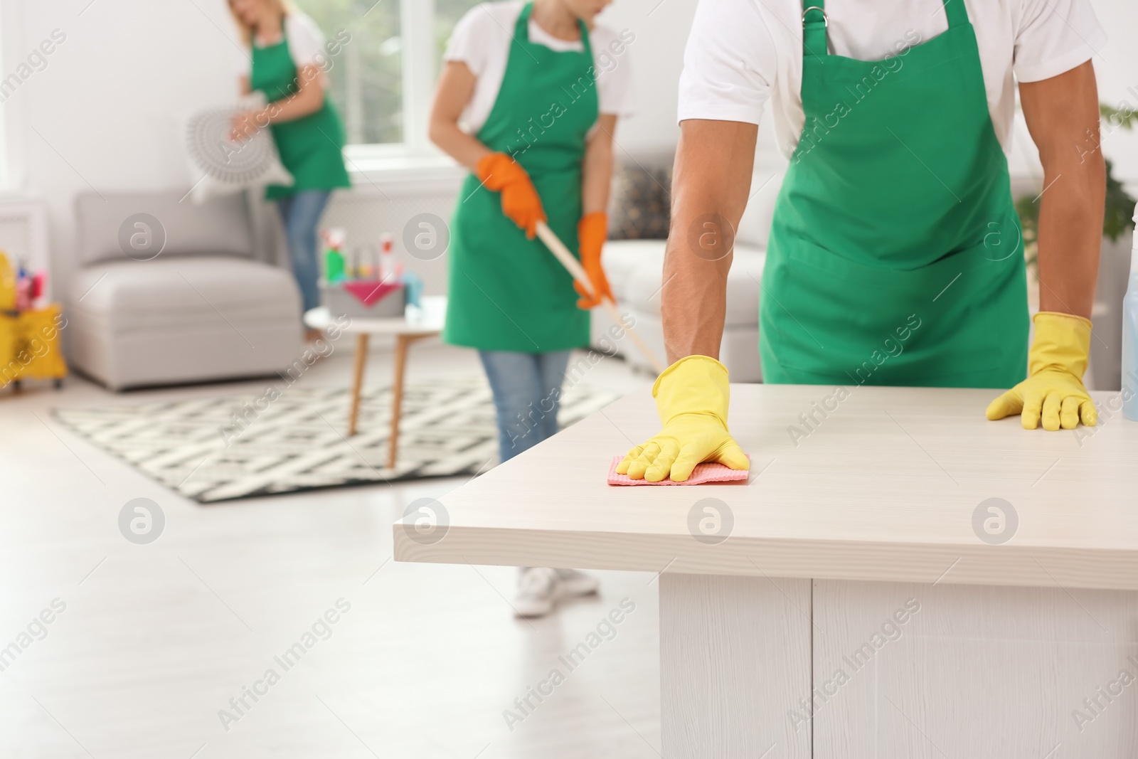 Photo of Man in gloves cleaning table indoors, closeup