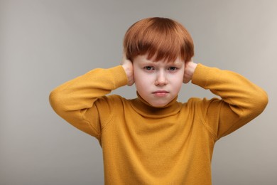 Hearing problem. Little boy suffering from ear pain on grey background