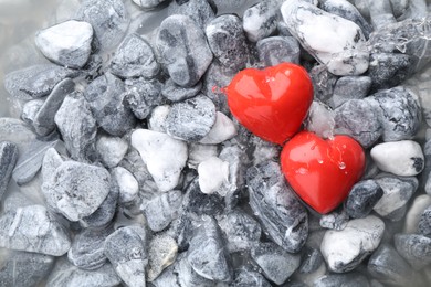 Red decorative hearts on stones and water, top view. Space for text