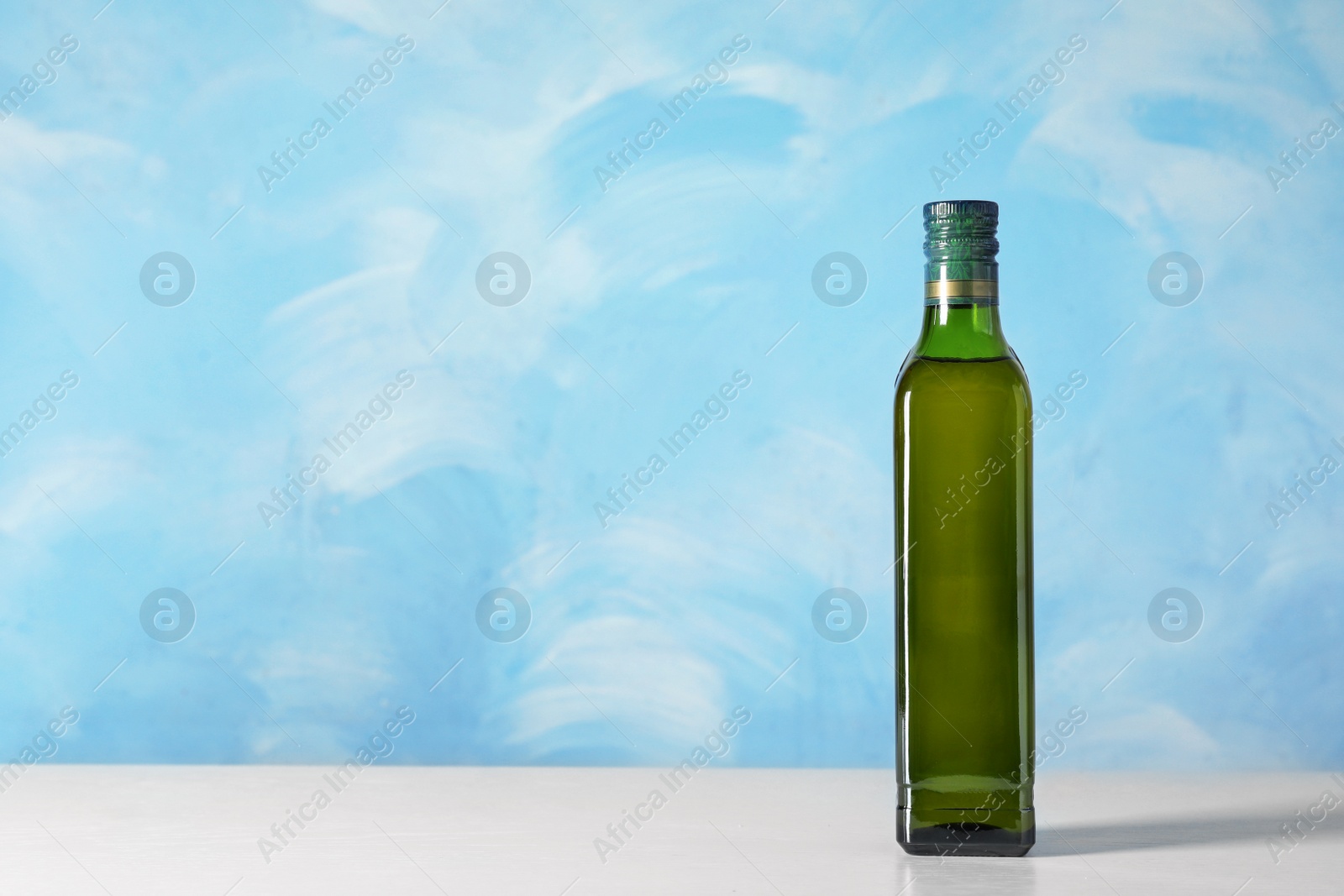 Photo of Bottle of oil on table against color background. Space for text