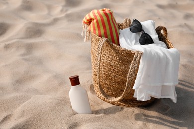 Photo of Beach bag, towel, blanket, sunglasses and sunscreen on sand, space for text