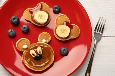 Photo of Creative serving for kids. Plate with cute bears made of pancakes, berries, banana and chocolate paste on white wooden table, flat lay