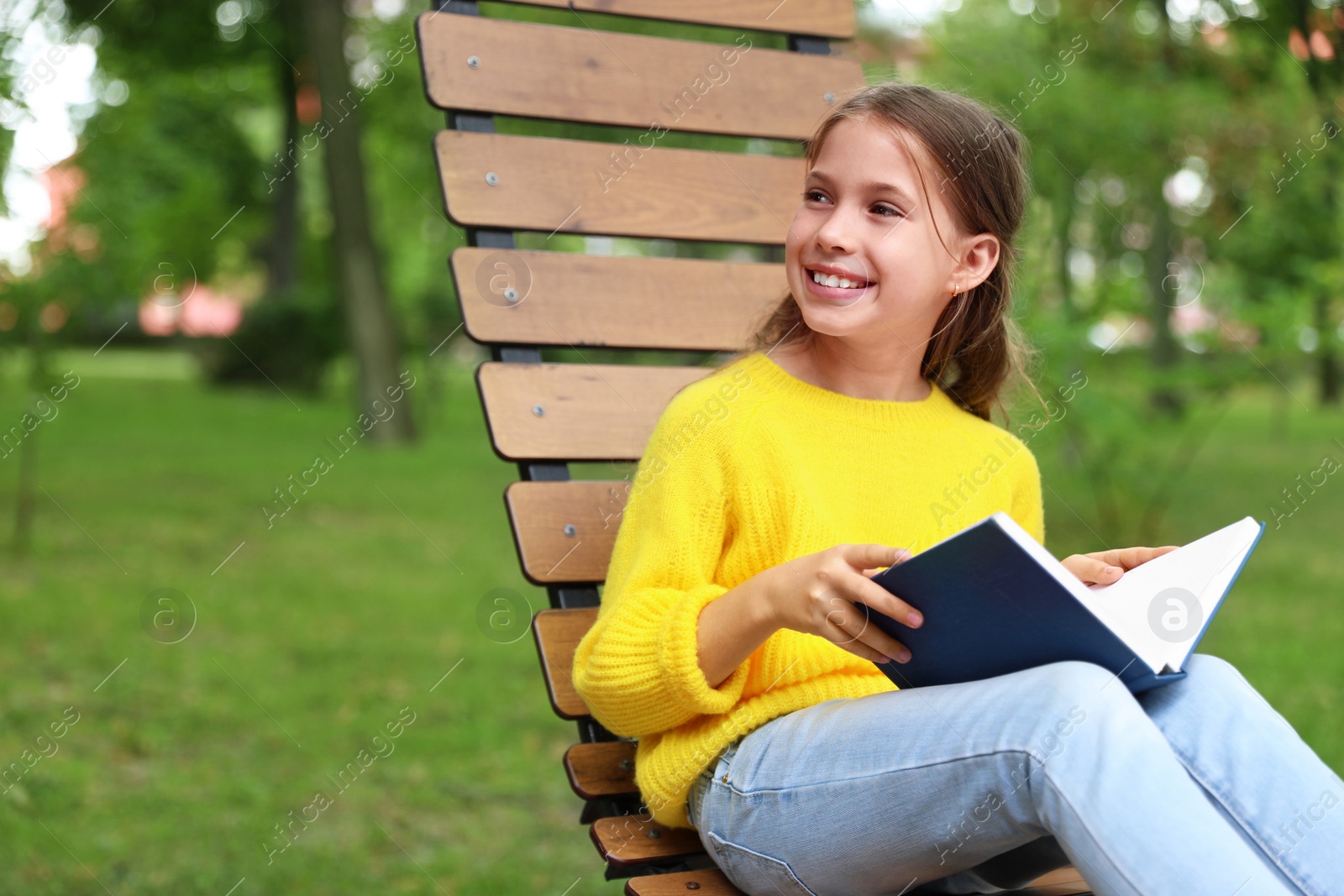 Image of Happy little girl reading book in park 