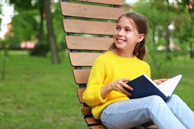 Image of Happy little girl reading book in park 