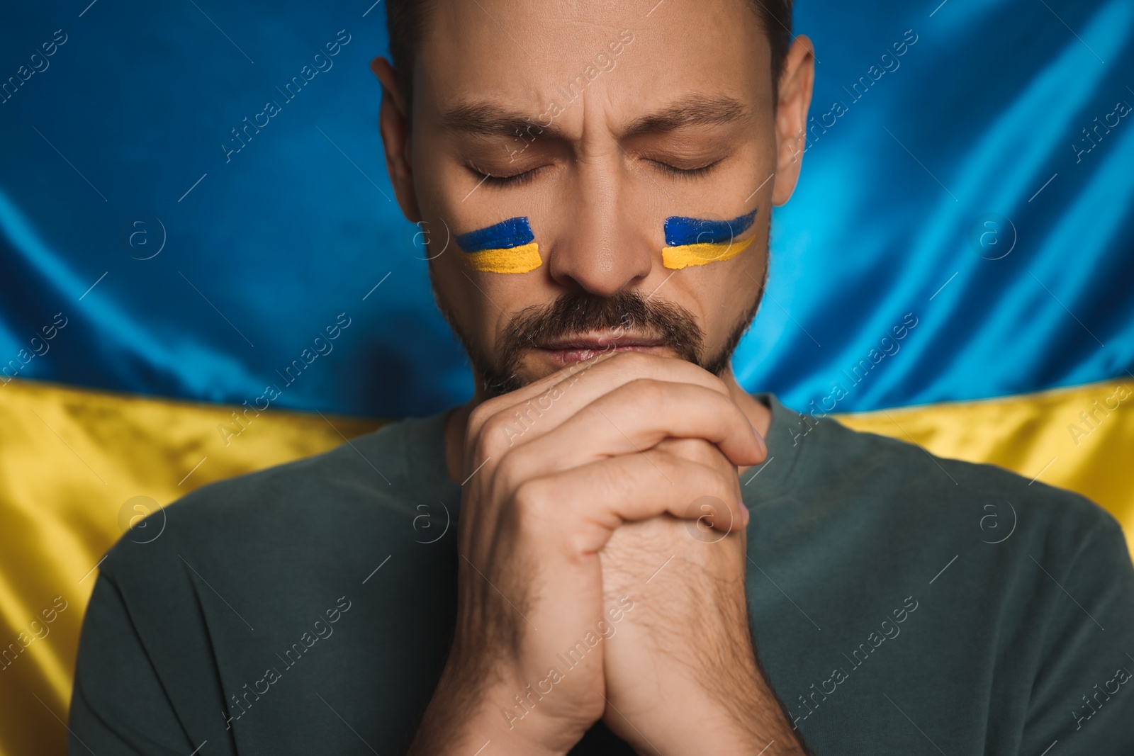 Photo of Man with clasped hands near Ukrainian flag, closeup