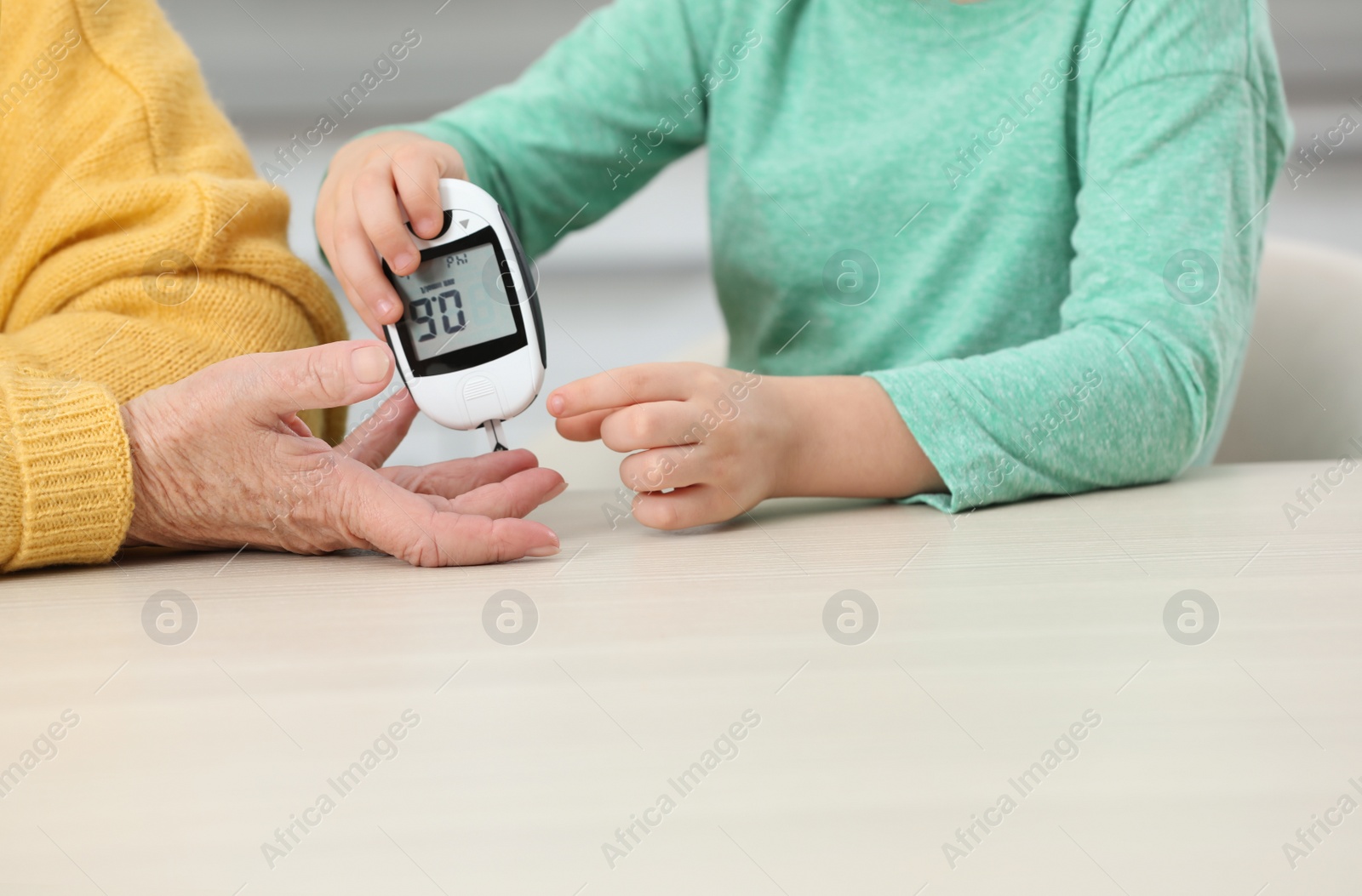 Photo of Senior woman with her grandson using digital glucometer at table, closeup. Diabetes control