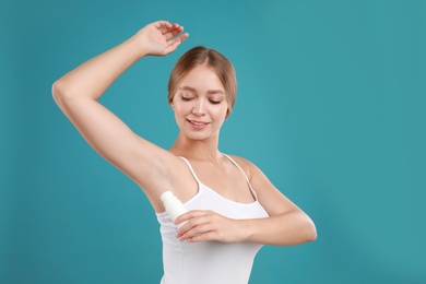 Photo of Young woman applying deodorant to armpit on teal background