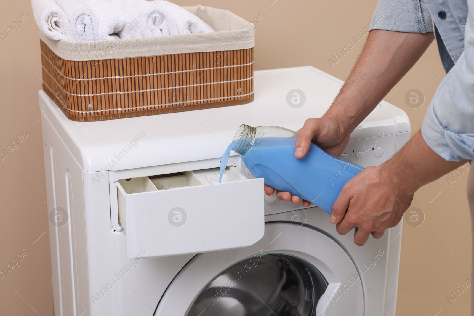 Photo of Man pouring fabric softener from bottle into washing machine indoors, closeup