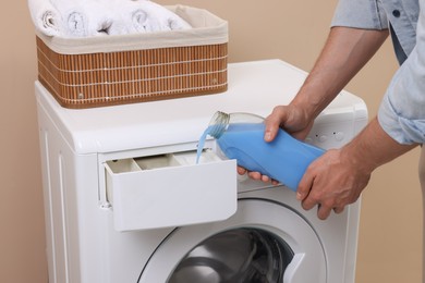 Photo of Man pouring fabric softener from bottle into washing machine indoors, closeup