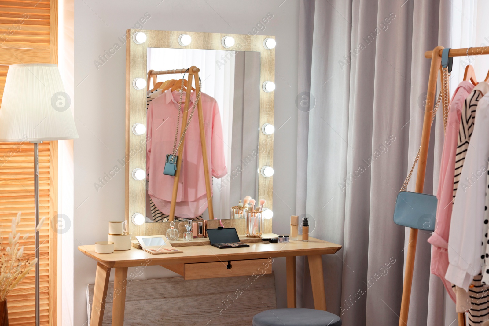 Photo of Makeup room. Stylish mirror and different beauty products on wooden dressing table indoors