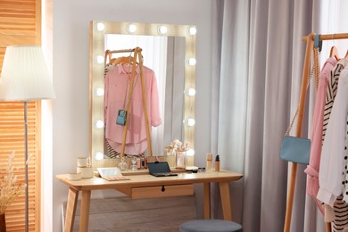 Makeup room. Stylish mirror and different beauty products on wooden dressing table indoors