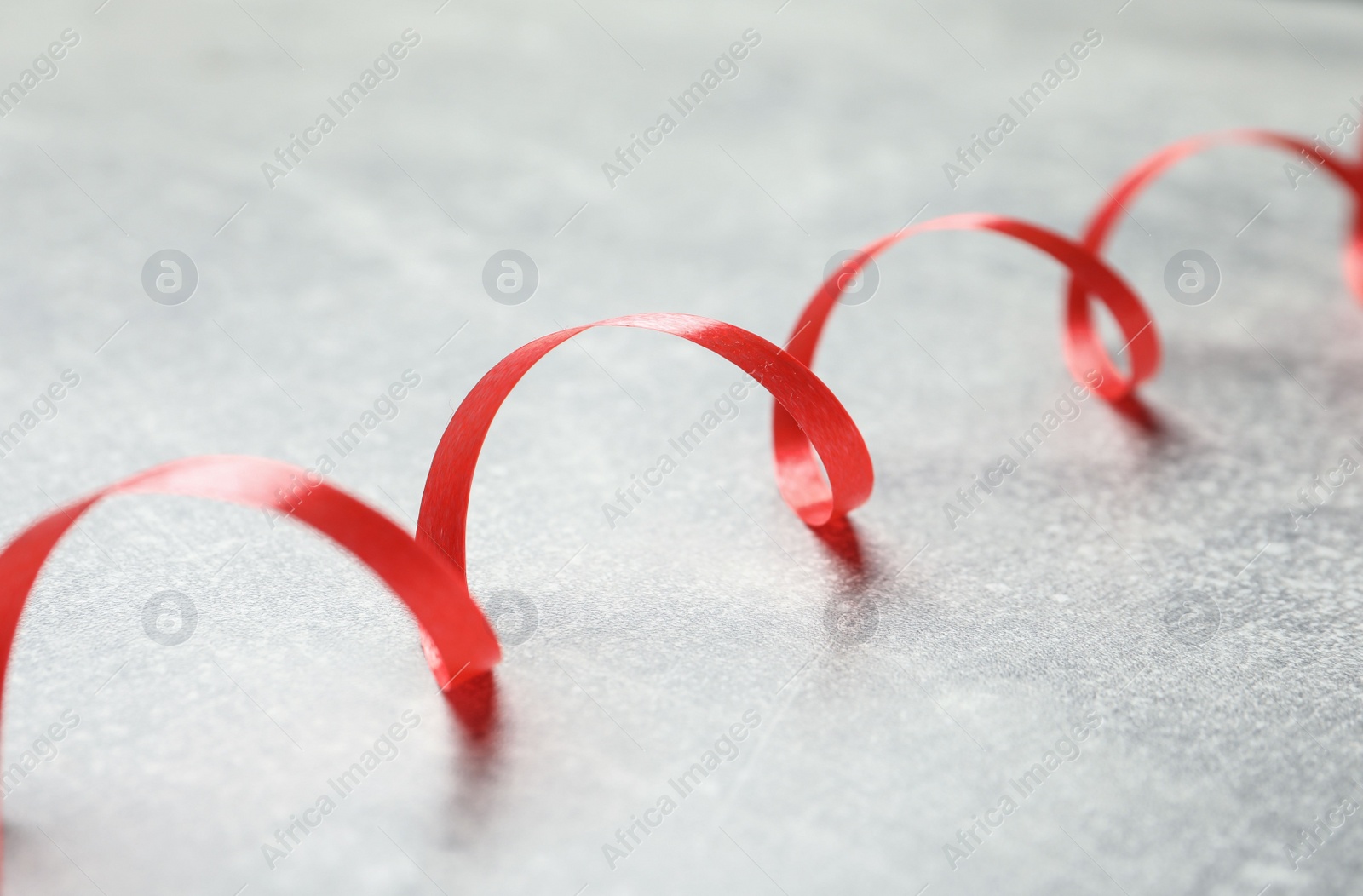 Photo of Shiny red serpentine streamer on grey background, closeup