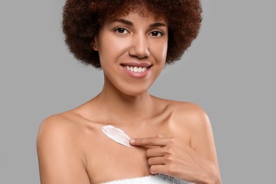 Photo of Beautiful young woman applying cream onto body on grey background