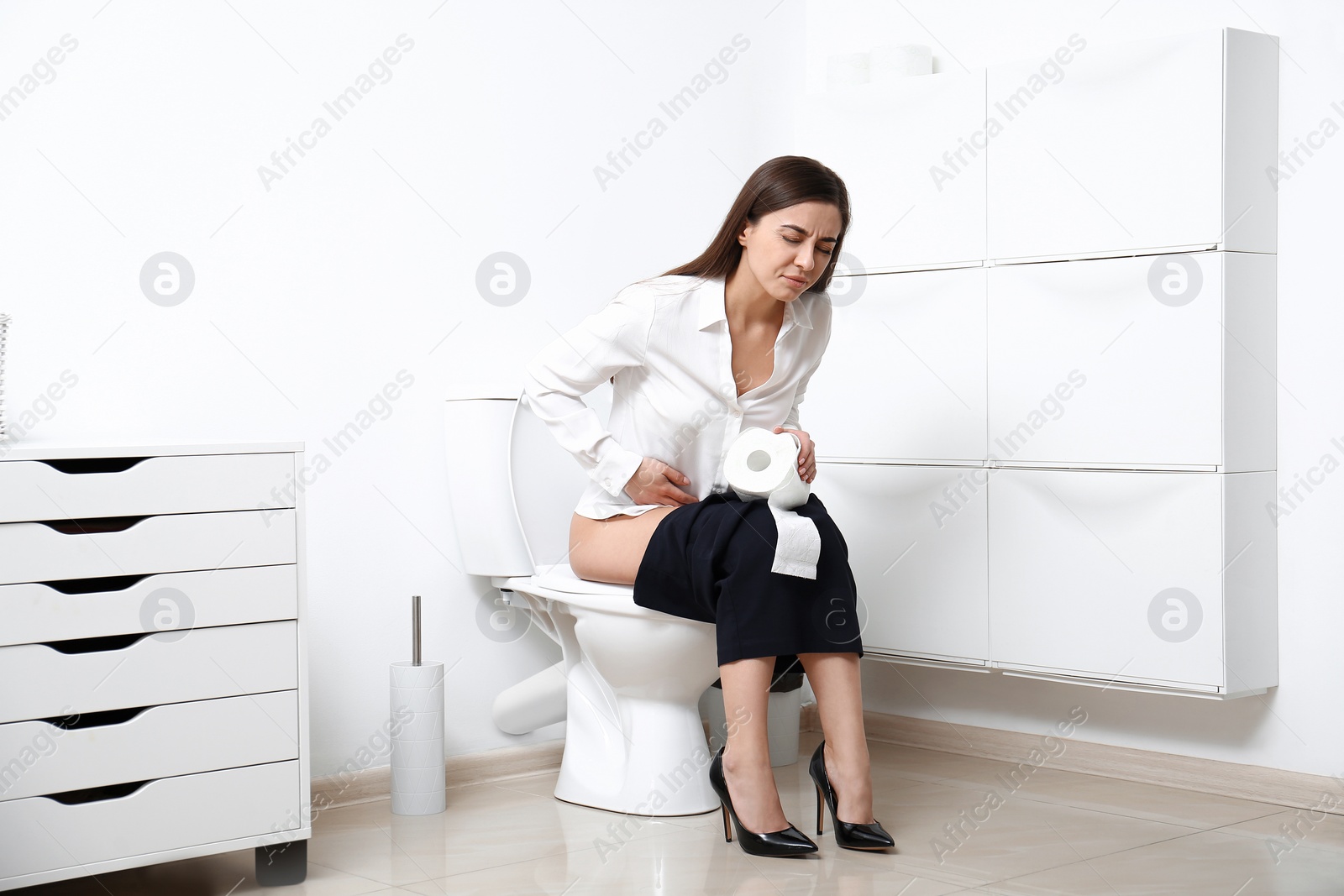 Photo of Woman with stomach ache sitting on toilet bowl in bathroom