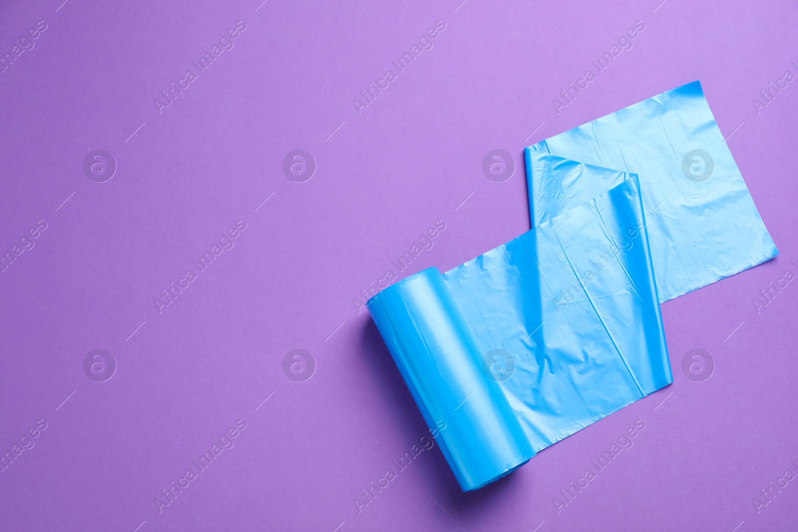 Photo of Roll of light blue garbage bags on violet background, top view. Space for text