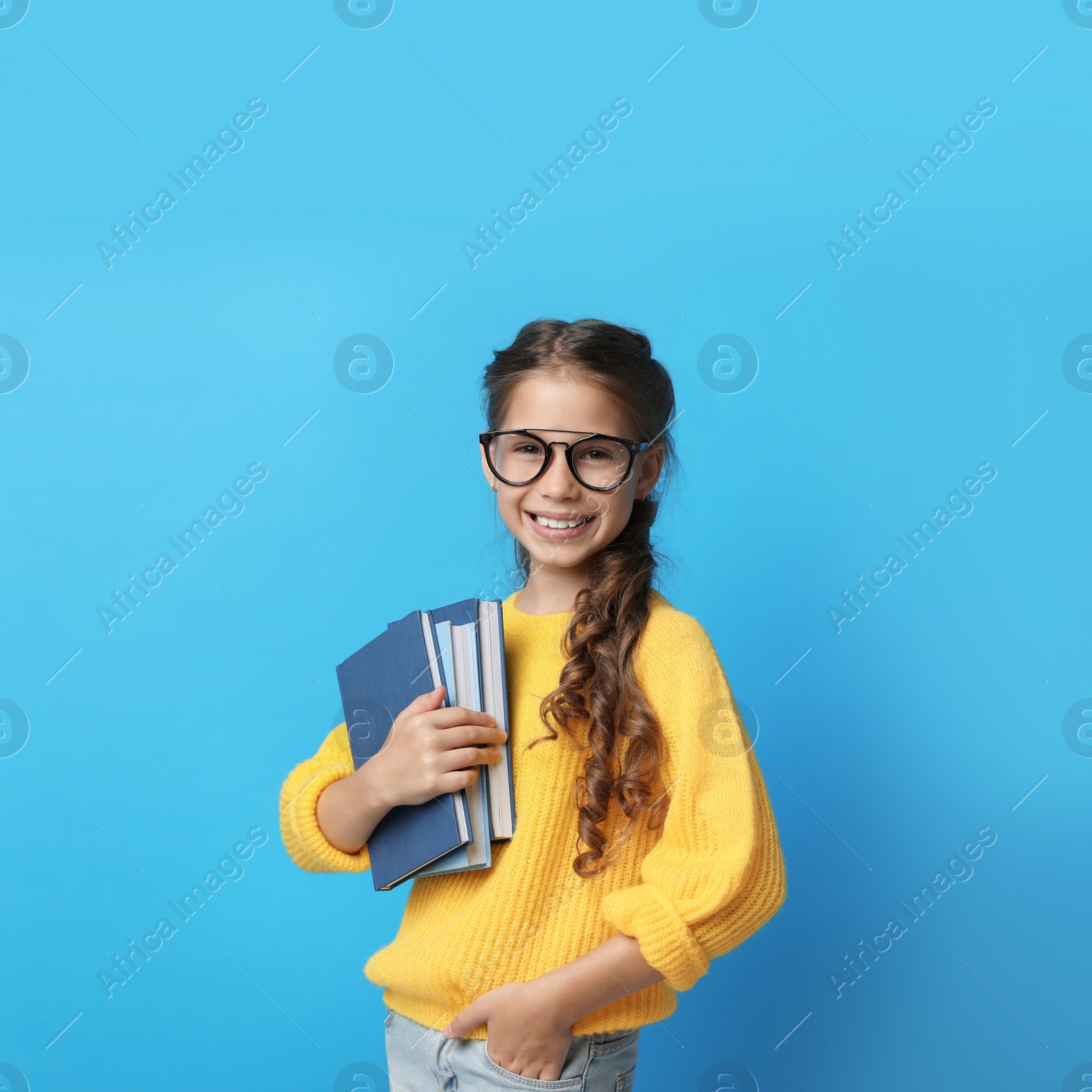 Photo of Cute little girl with glasses and books on blue background. Reading concept