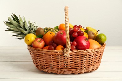 Wicker basket with different fresh fruits on white wooden table