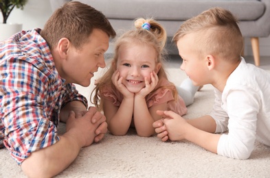Cute little children and their father lying on cozy carpet at home