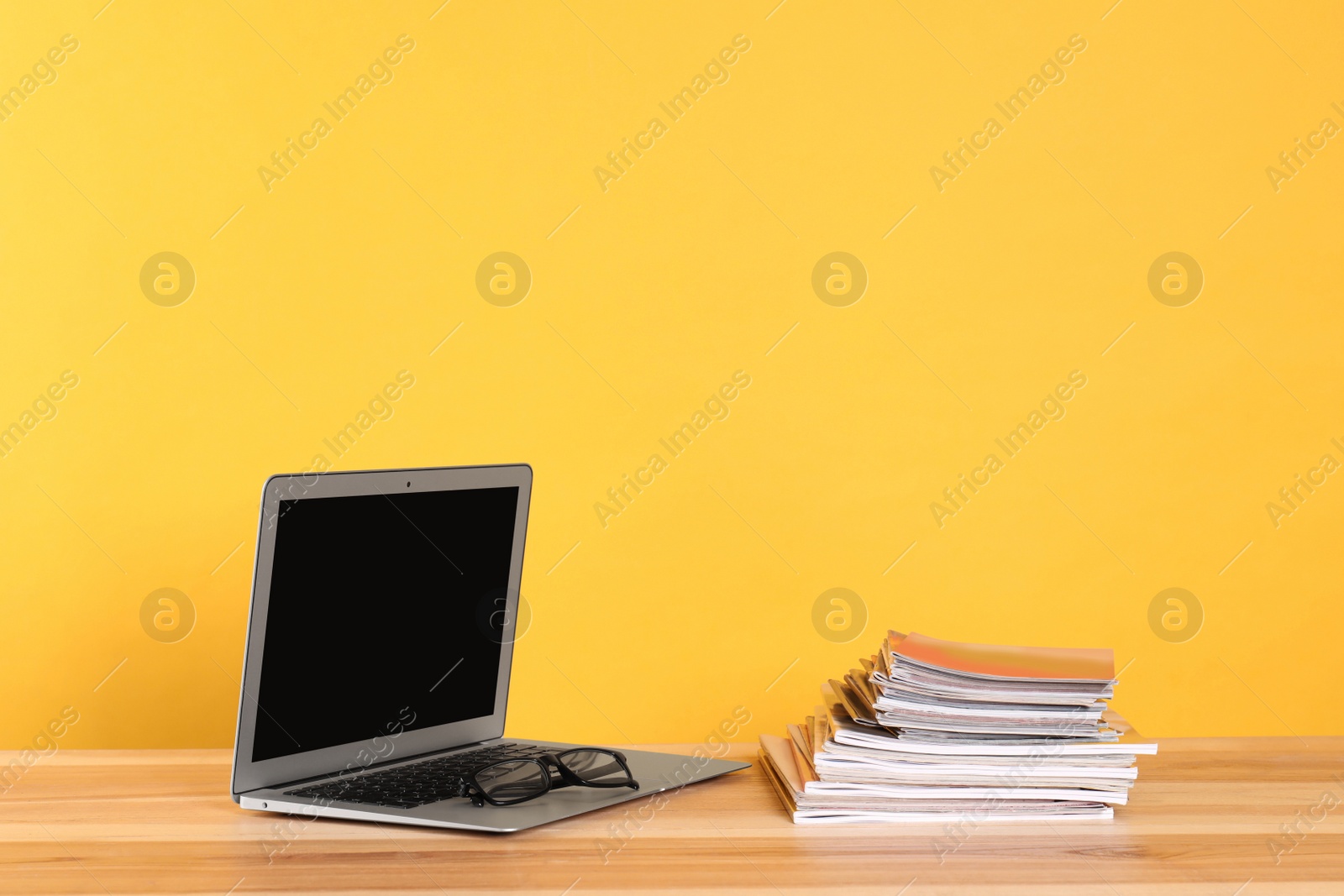 Photo of Laptop, glasses and stack of magazines on wooden table. Space for text