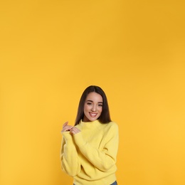 Photo of Beautiful young woman wearing warm sweater on yellow background. Space for text