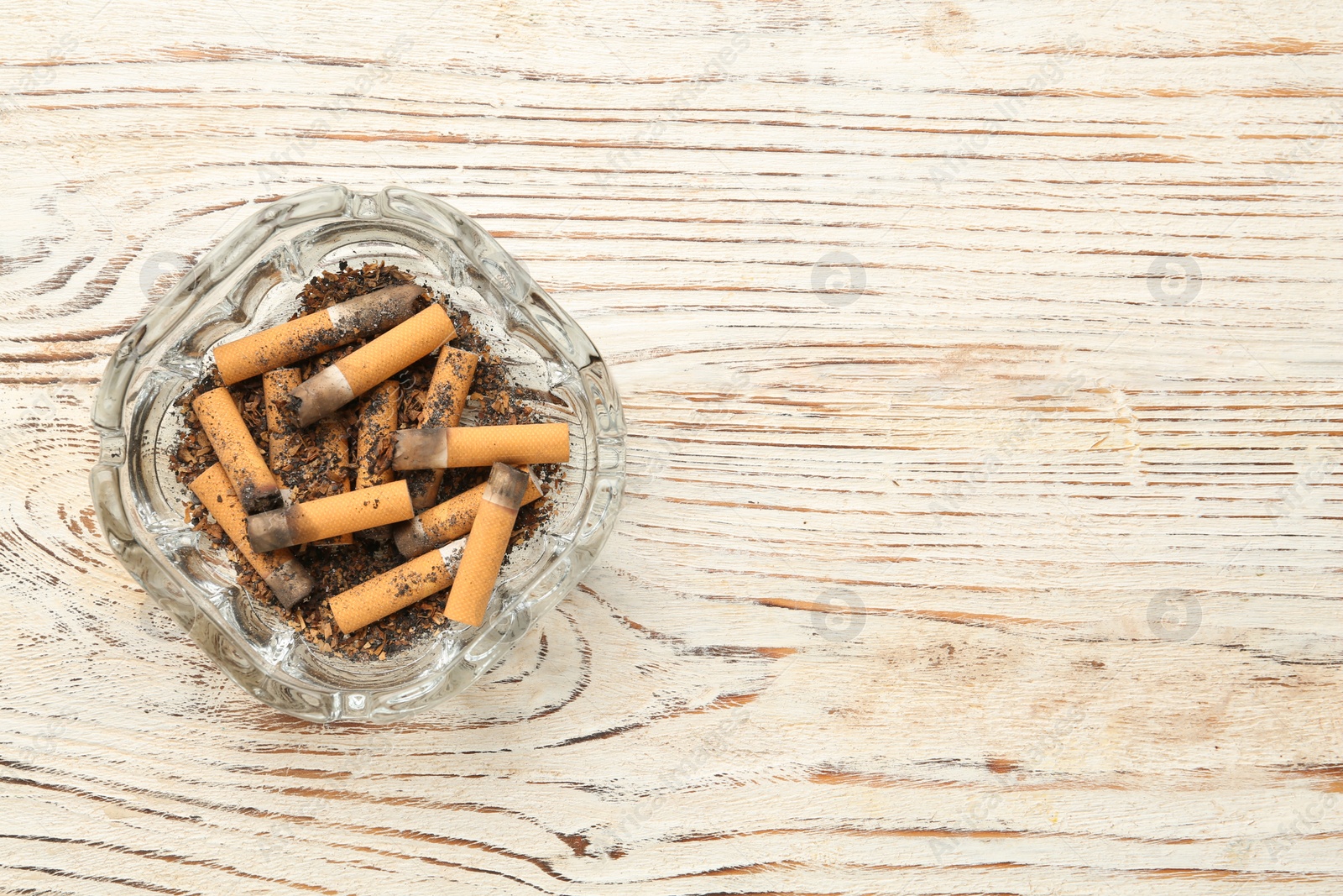 Photo of Glass ashtray with cigarette stubs on white wooden table, top view. Space for text