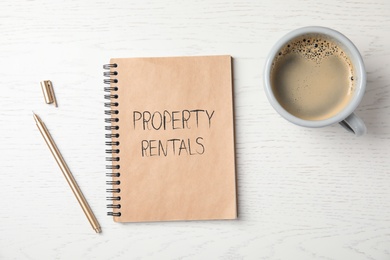 Notebook with text Property Rentals, cup of coffee and pen on white wooden table, flat lay 