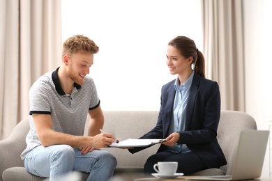 Young man signing contract with female insurance agent in office