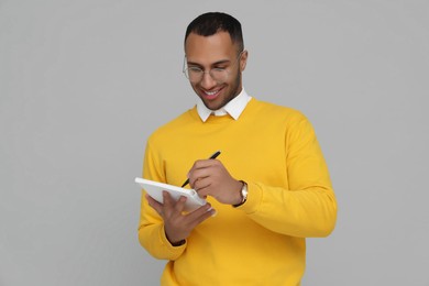 Happy young intern writing in notebook on light grey background