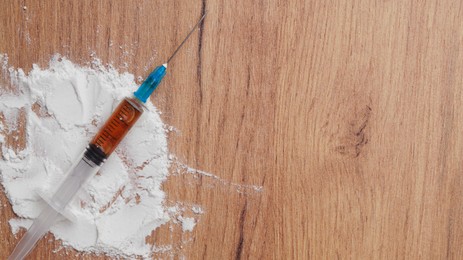 Powder and syringe on wooden table, flat lay with space for text. Hard drugs