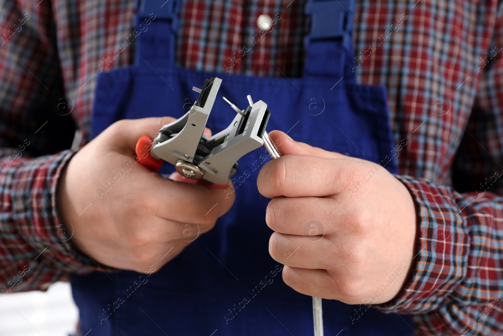 Photo of Professional electrician in uniform stripping wiring, closeup view