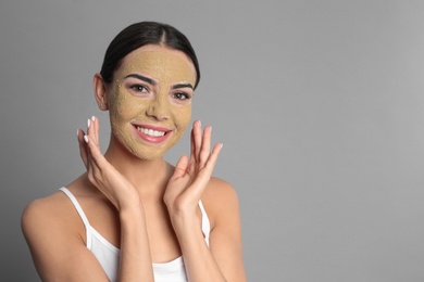 Photo of Young woman with clay mask on her face against grey background, space for text. Skin care