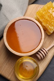 Photo of Sweet honey in bowls, dipper and pieces of honeycomb on grey table, flat lay