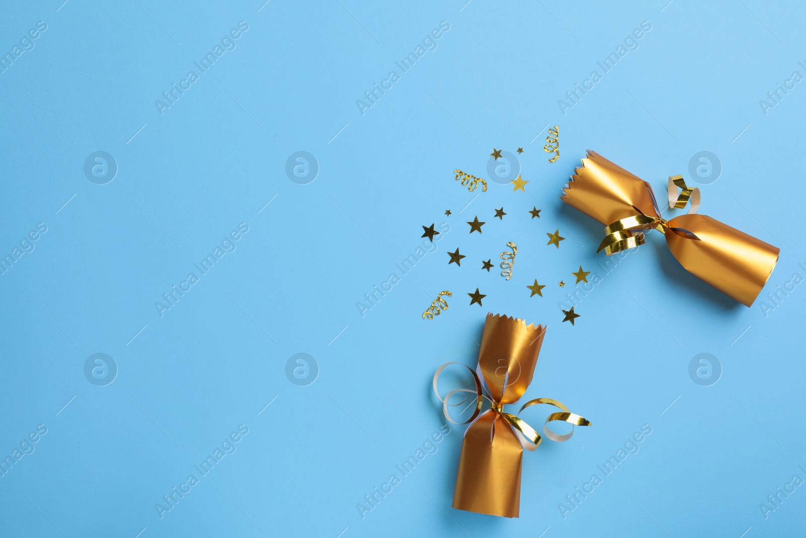 Photo of Open golden Christmas cracker with shiny confetti on light blue background, top view. Space for text