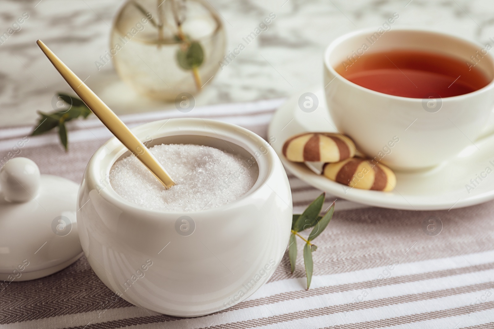 Photo of Granulated sugar in bowl and aromatic tea on table