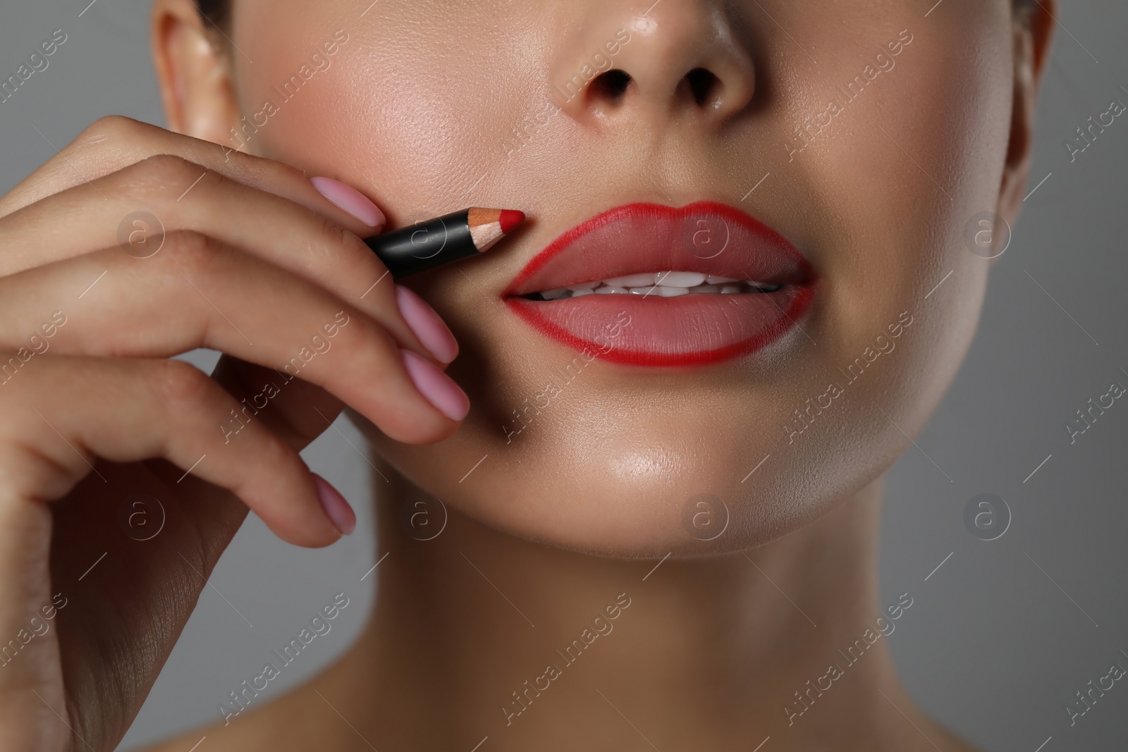 Photo of Young woman with beautiful red lip pencil on grey background, closeup