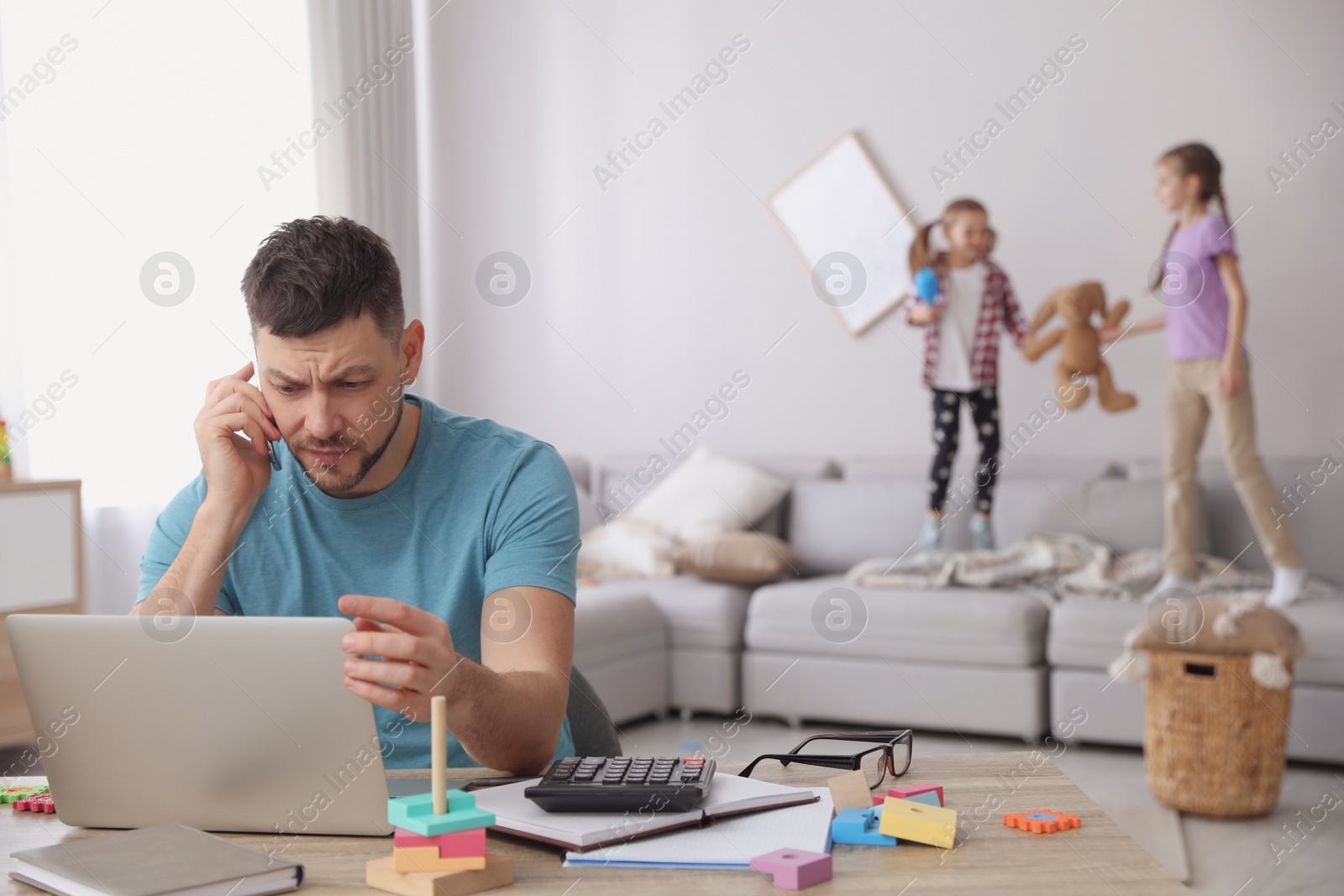 Photo of Children disturbing stressed man in living room. Working from home during quarantine